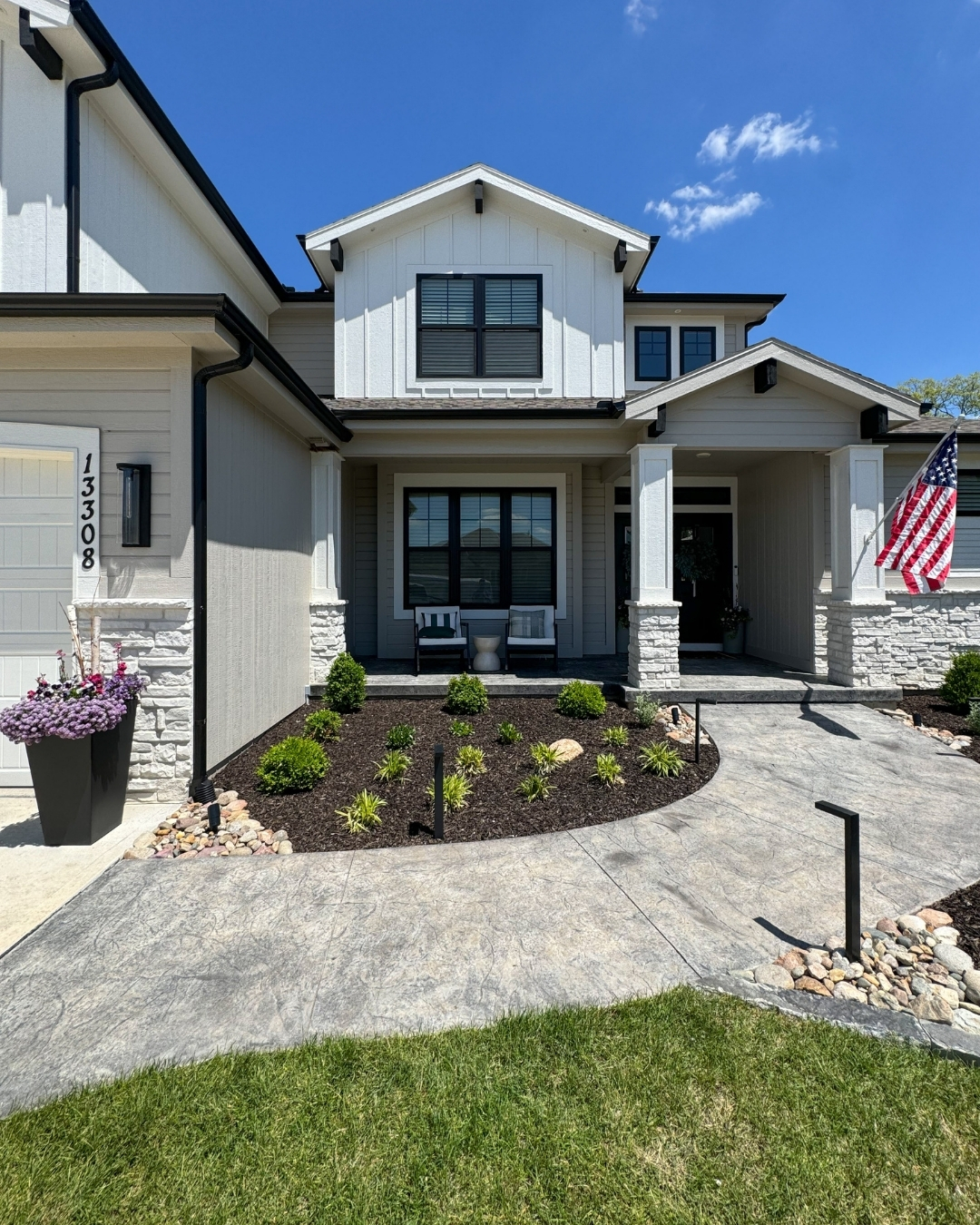 Front yard with stamped concrete walkway, dark mulch bed and American flag