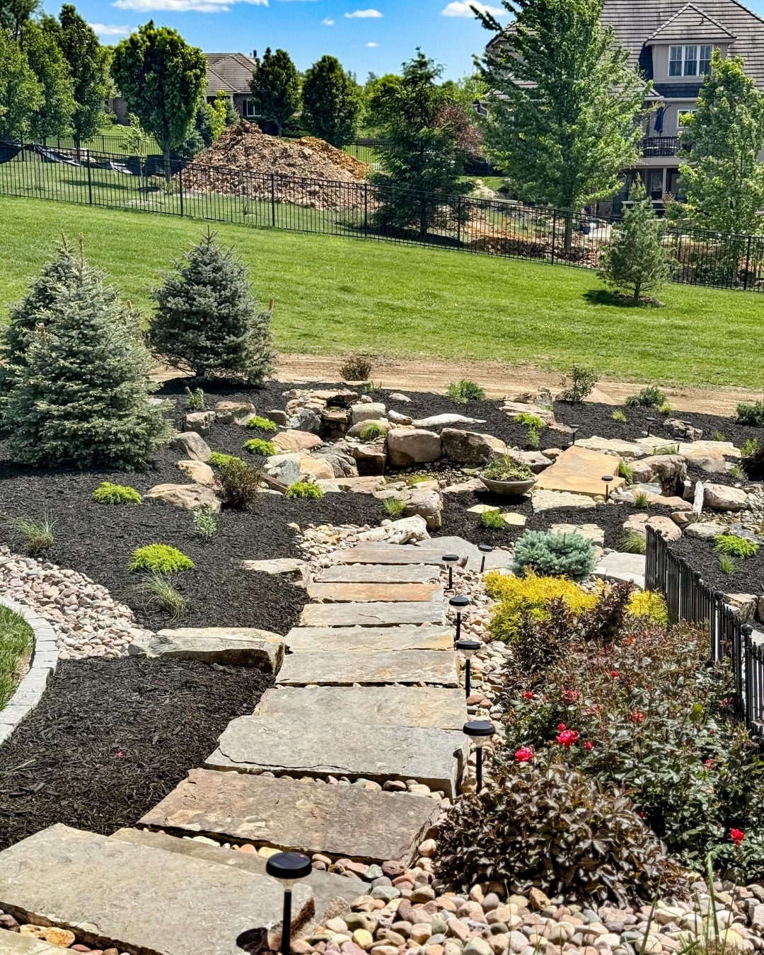 Flagstone stepping stone path through a boulder and mulch landscape with evergreens