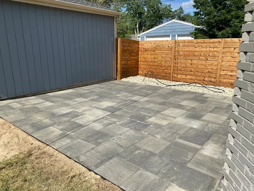 Modern gray paver patio beside a garage with cedar privacy fence