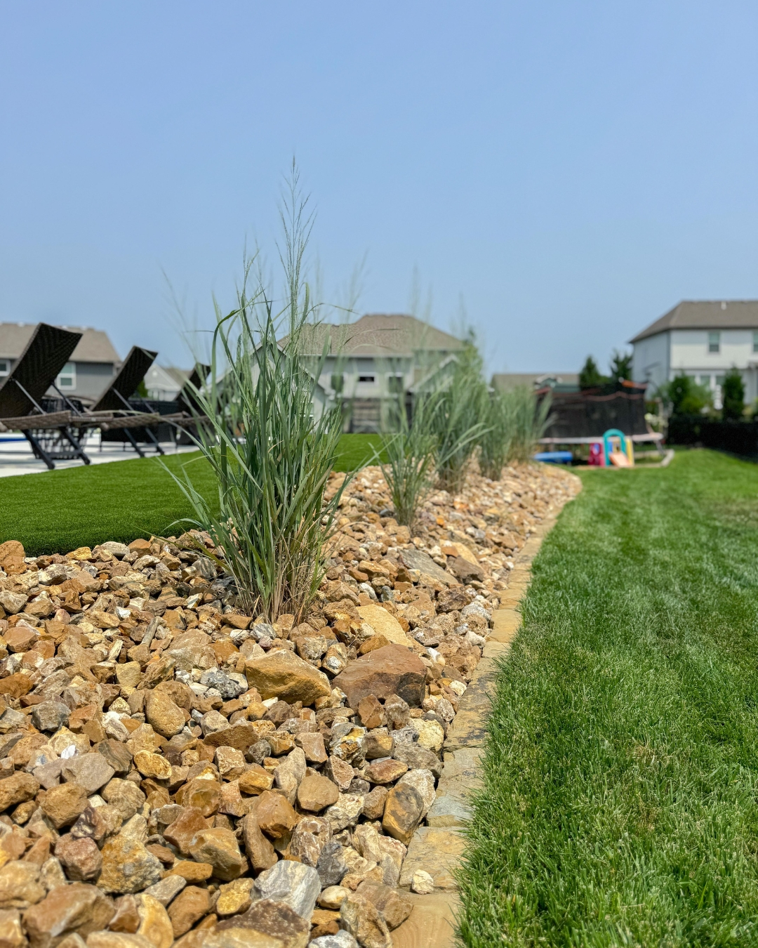 Stone-edged rock bed with ornamental grasses separating turf and lawn