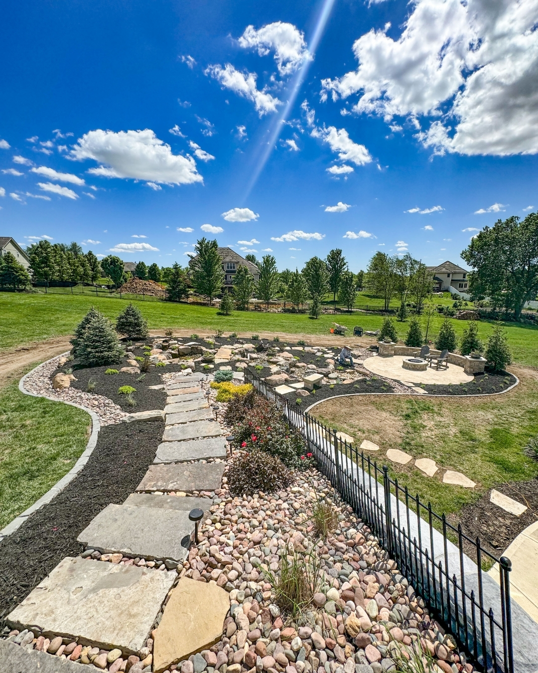 Large backyard rock garden with flagstone path, boulders and a paver fire pit patio