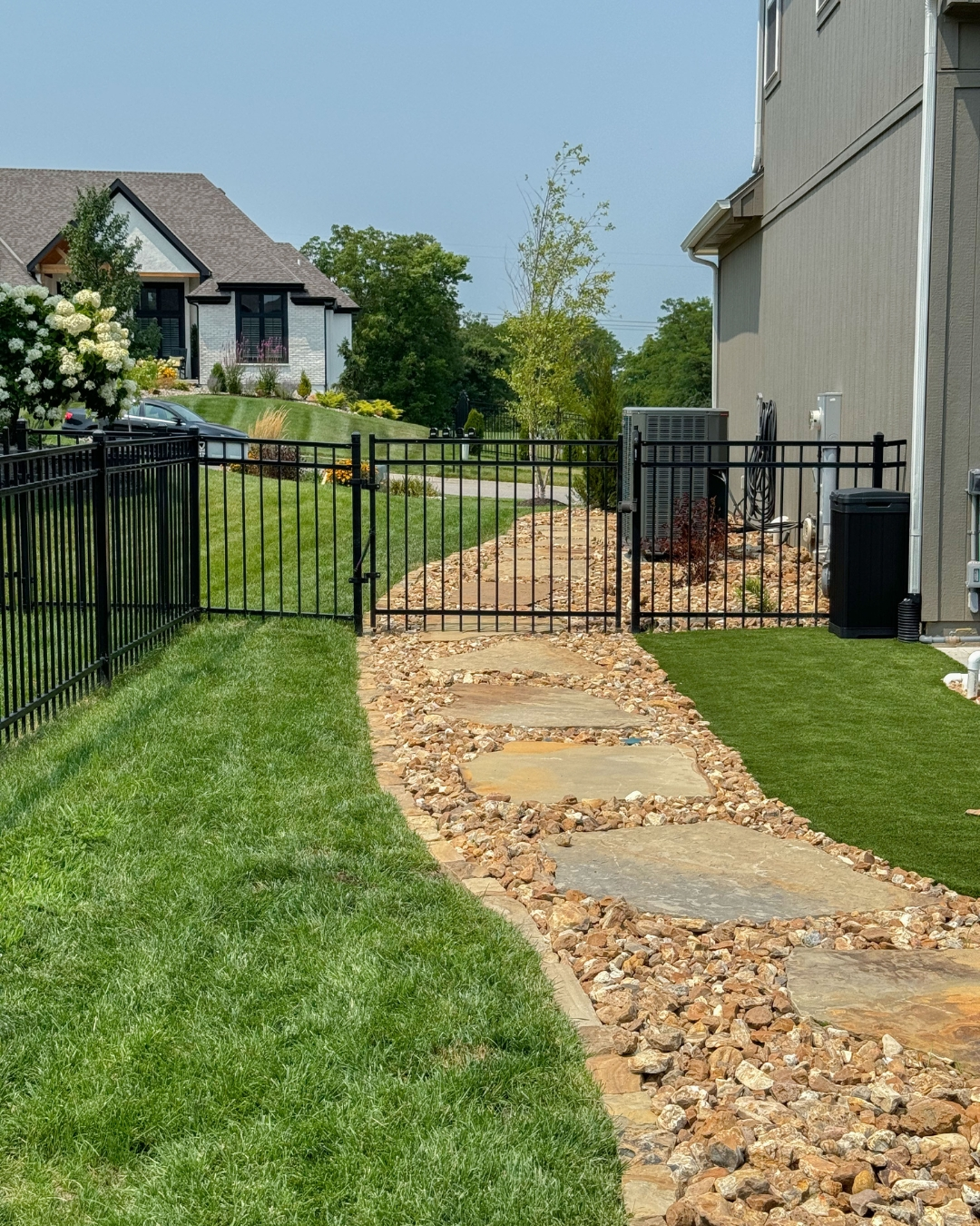 Flagstone walkway with rock border between a fenced lawn and house