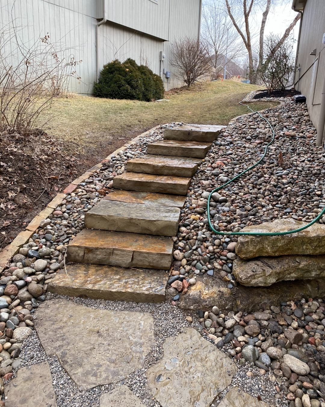 Natural stone step installation with river rock beds beside a home