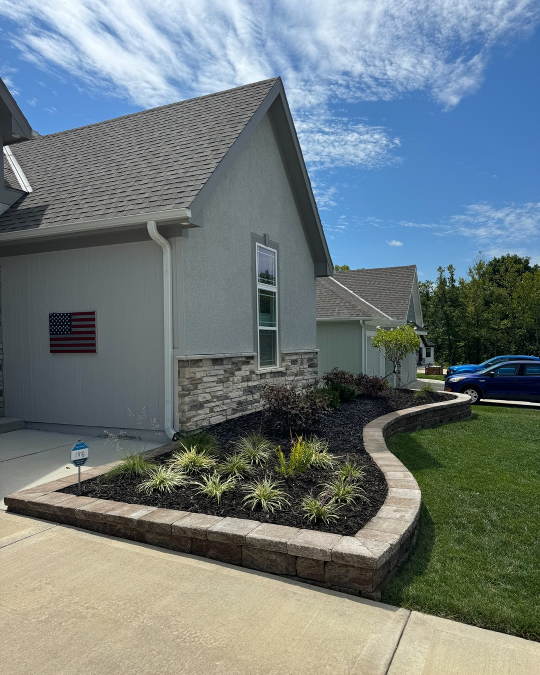 Curved stone retaining wall with black mulch bed and ornamental grasses along a home